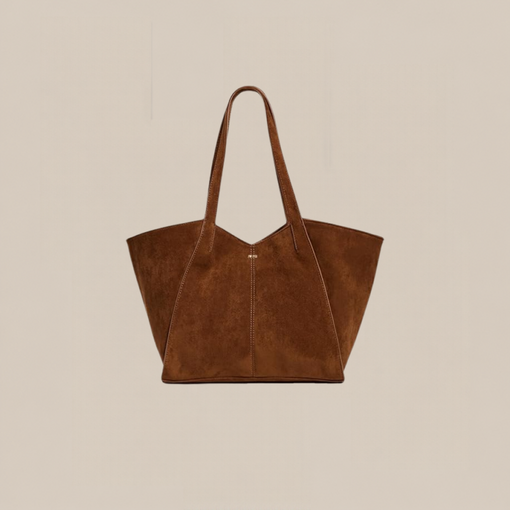 Brown suede tote bag with two long handles on a neutral beige background Tldr winter work outfits are easier with seven closet staples kick crop pants office shoes in the same color a button down a merino sweater a third piece weatherproof boots and a work tote Pair the pants and shoes in one color then build the top half around a button down and a merino sweater with a  adjust my crown